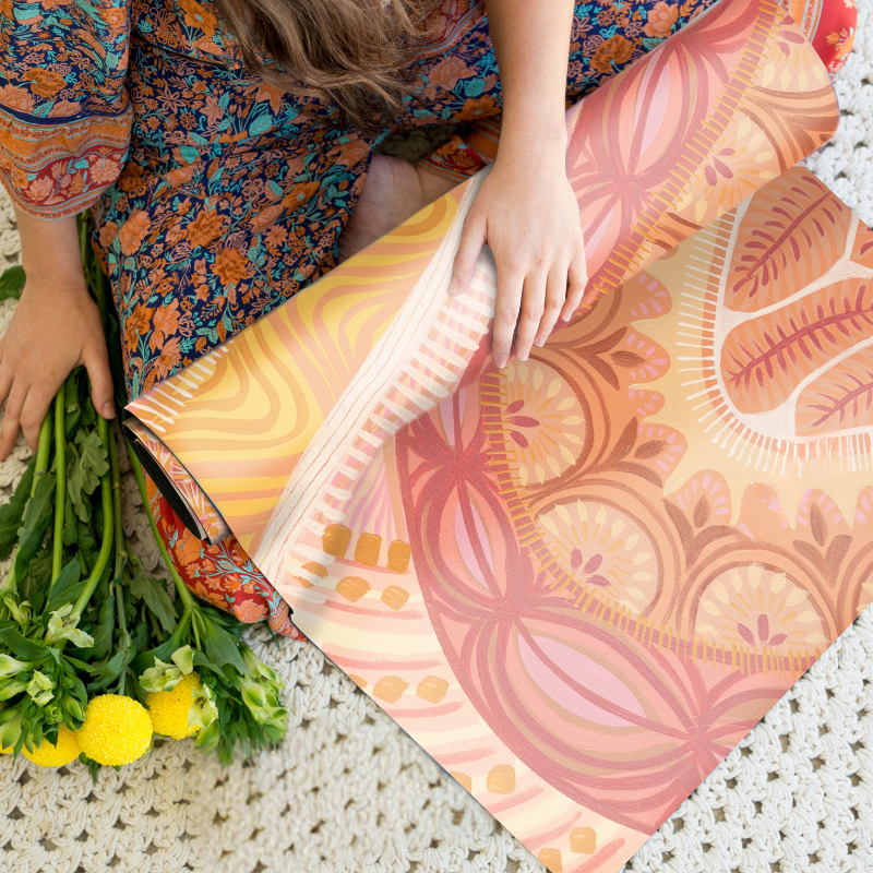 The Indie yoga mat laid out on a cozy surface, showcasing its artistic floral design in warm, earthy tones, surrounded by natural decor and a serene setting.

